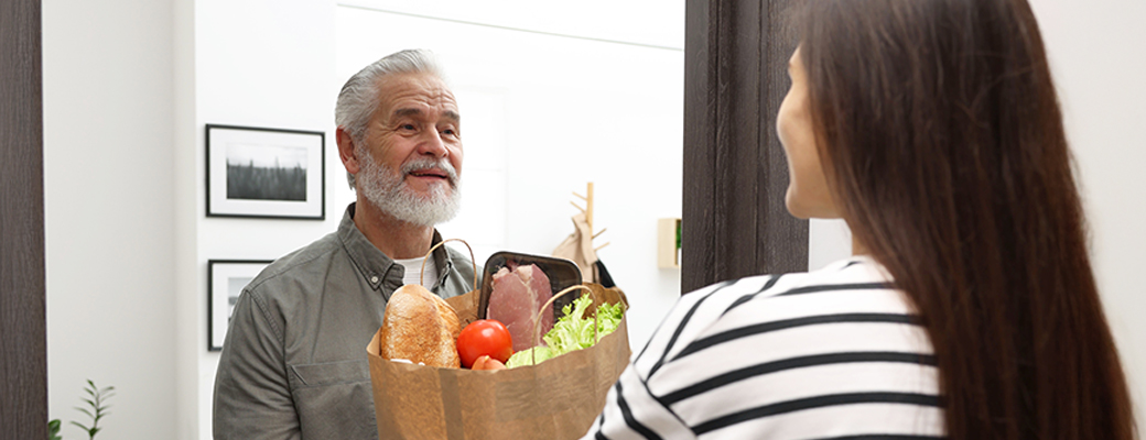 Image of woman delivering a bag of groceries to the door of a senior man